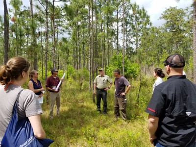 ANREP workshop participants gather around a speaker in a field
